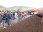 People all standing along a mound of soil, learning about compost